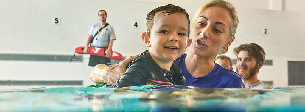 a woman holding a baby in the water helping him learn how to swim at the ymca