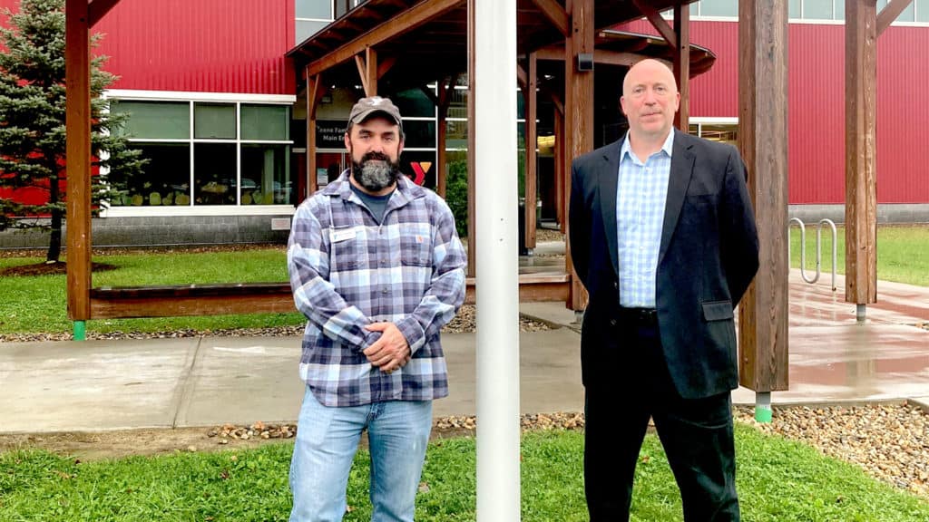 Matt Primrose (left) and Dan Smith (right) stand next to the new flagpole at the YMCA entrance