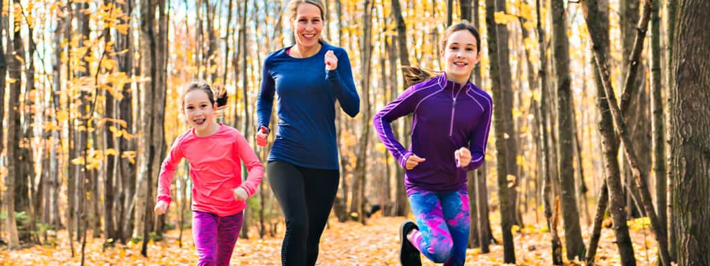 a women and two kids running through the fall woods