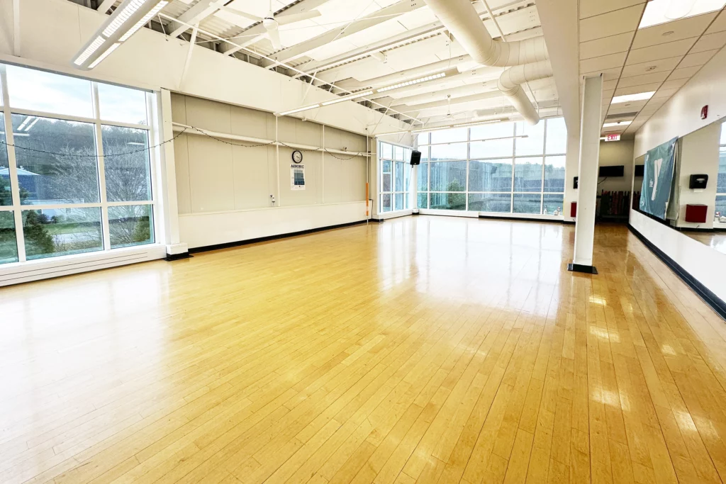 a large studio with mirrored walls, large floor to ceiling windows and a hardwood floor