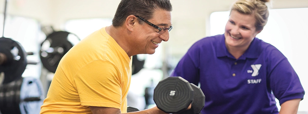 man lifting a dumbell at the keene ymca while a trainer stands by