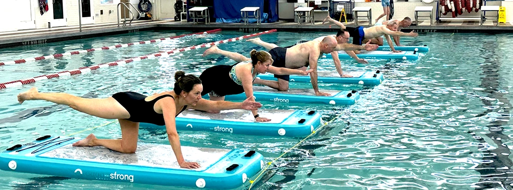 several participants balancing on water boards during a liquid gym class at the Y