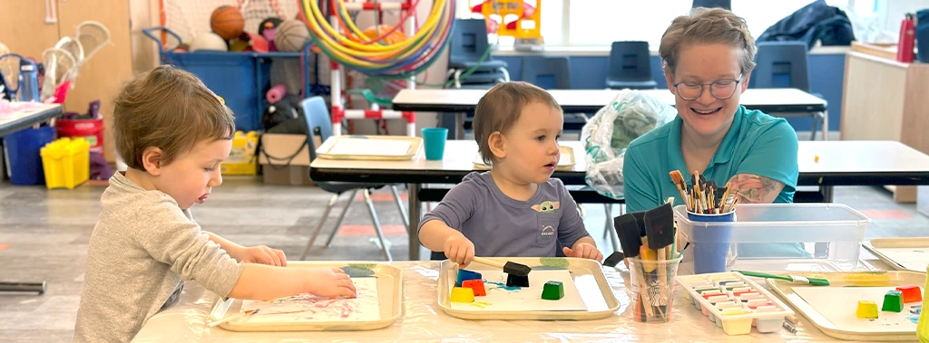 two small children with instructor finger painting in birght classroom setting